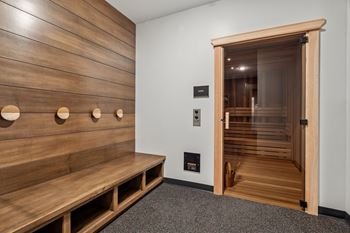 A wooden bench with circular cutouts on the back is in a room with a wooden wall and a door.